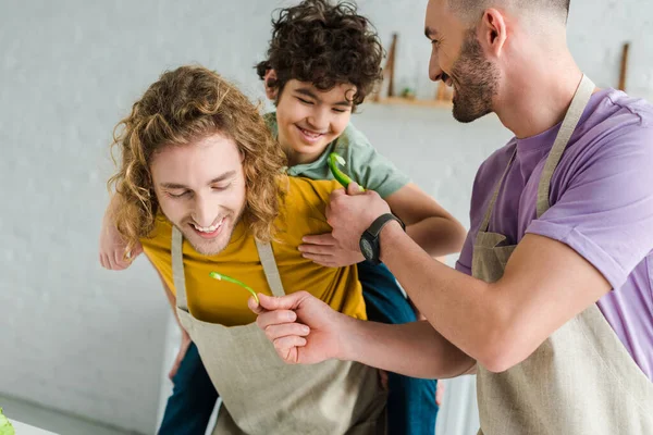 Happy homosexual father holding bell pepper near partner and mixed race son — Stock Photo