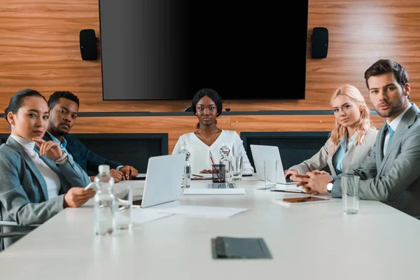 Молодые, уверенные в себе мультикультурные бизнесмены сидят в конференц-зале с ЖК-экраном на стене — стоковое фото