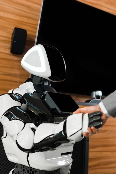 Частковий вигляд бізнесмена, що тремтить руками з гуманоїдним роботом в офісі — стокове фото