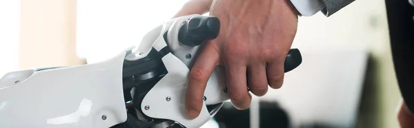 Cropped view of businessman and robot shaking hands in office, panoramic shot — Stock Photo