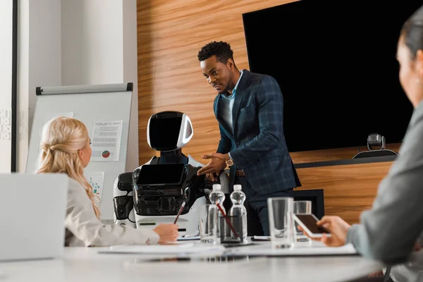 Bell'uomo d'affari afro-americano che punta il dito contro il robot vicino ai colleghi nella sala conferenze — Foto stock