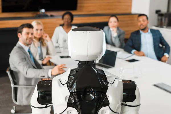 Selective focus of multicultural businesspeople looking at robot in conference hall — Stock Photo