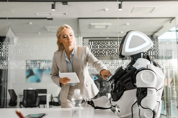 Attraktive Geschäftsfrau hält digitales Tablet während sie Roboter bedient — Stockfoto