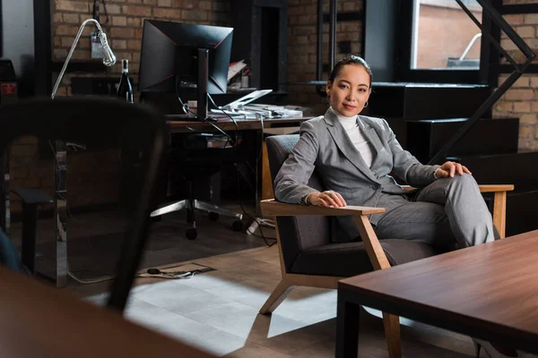 Foco seletivo de atraente asiático empresária sentado em poltrona no escritório moderno — Fotografia de Stock