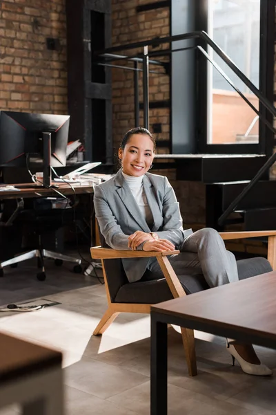 Foyer sélectif de attrayant asiatique femme d'affaires assis dans le fauteuil et souriant à la caméra — Photo de stock