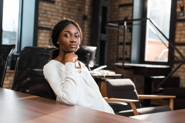 Pensativa, mulher de negócios americana africana grávida sentada na mesa de escritório e olhando para a câmera — Fotografia de Stock