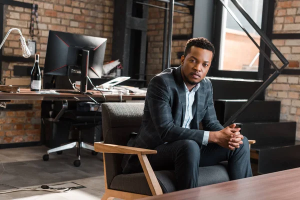 Впевнений афроамериканський бізнесмен сидить у кріслі й дивиться на камеру. — стокове фото