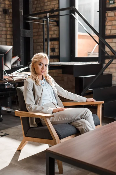 Attraktive, nachdenkliche Geschäftsfrau, die im Sessel sitzt und in die Kamera blickt — Stockfoto