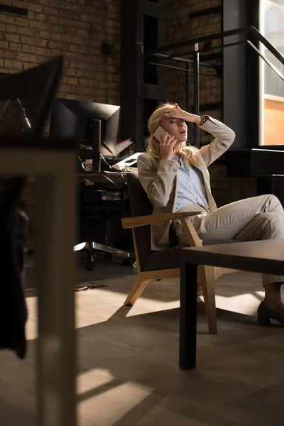 Selective focus of tired business woman talking on smartphone while suffering from headache — Stock Photo