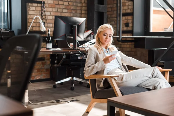 Attraktive konzentrierte Geschäftsfrau sitzt im Sessel und plaudert auf dem Smartphone — Stockfoto