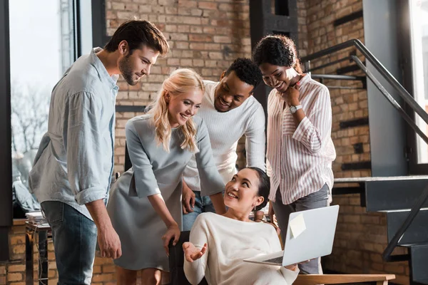 Happy asian businesswoman with laptop looking at smiling multicultural colleagues — Stock Photo