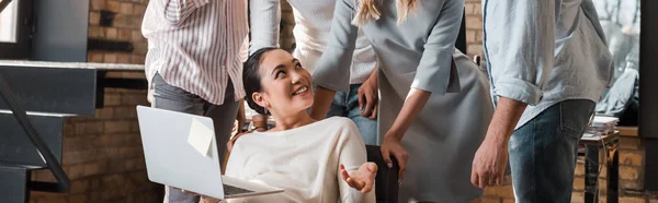 Cropped view of multicultural businesspeople looking at cheerful asian colleague sitting with laptop — Stock Photo