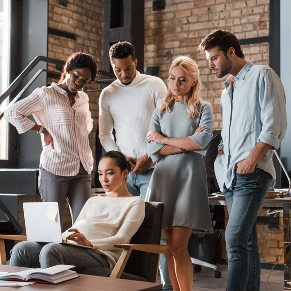 Serious multicultural businesspeople looking at asian colleague working on laptop — Stock Photo