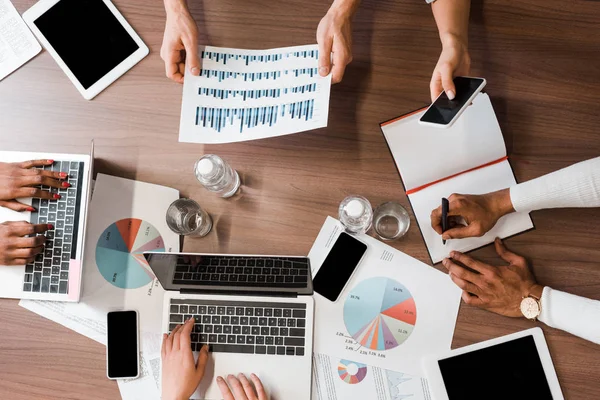 Cropped view of multicultural businesspeople working with gadgets and documents, top view — Stock Photo