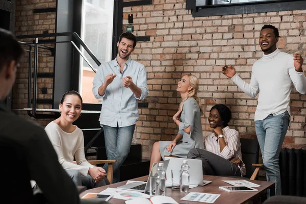 Alegres empresarios multiculturales haciendo gestos mientras discuten ideas de negocios en la oficina - foto de stock