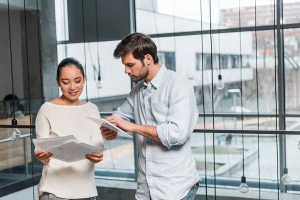 Young handsome businessman with digital tablet standing near attractive asian colleague holding documents — Stock Photo