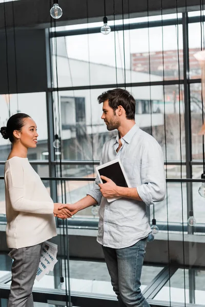 Young handsome businessman holding digital tablet while shaking hands with pregnant asian colleague — Stock Photo