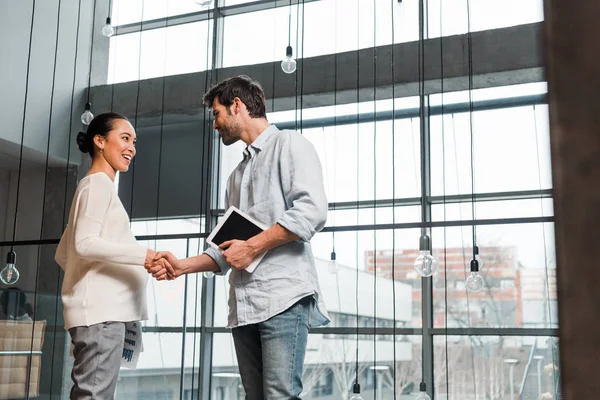 Young handsome businessman holding digital tablet while shaking hands with pregnant asian colleague — Stock Photo