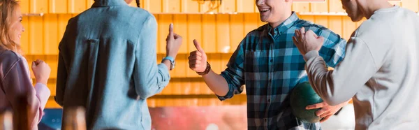 Cropped view of multicultural friends talking and showing thumbs up in bowling club — Stock Photo
