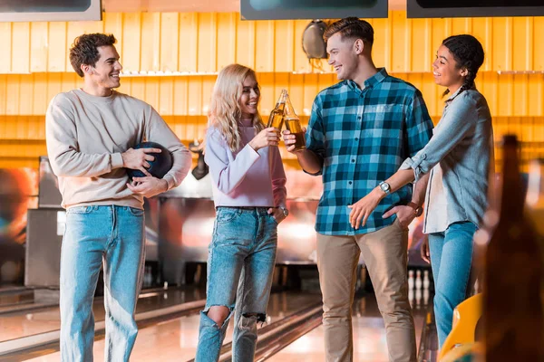Happy multicultural friend talking and clinking bottles of beer in bowing club — Stock Photo