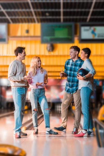 Smiling multicultural friend talking and drinking beer in bowing club — Stock Photo