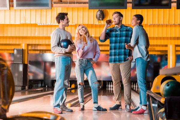 Cheerful multicultural friend talking and drinking beer in bowing club — Stock Photo