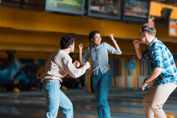 Excité afro-américaine fille avec ami multiculturel montrant des gestes gagnants au bowling club — Photo de stock