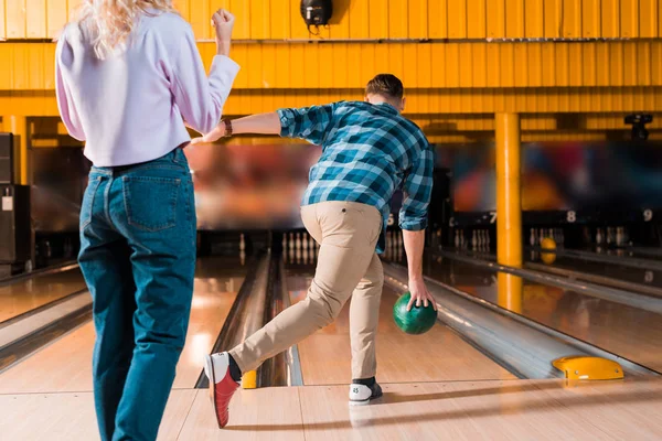 Vista cortada de menina de pé perto do homem jogando bola de boliche no beco skittle — Fotografia de Stock