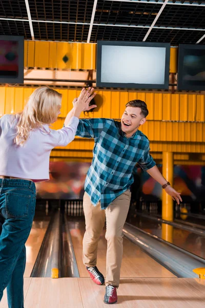 Happy couple giving high five while standing on skittle alley in bowling club — Stock Photo