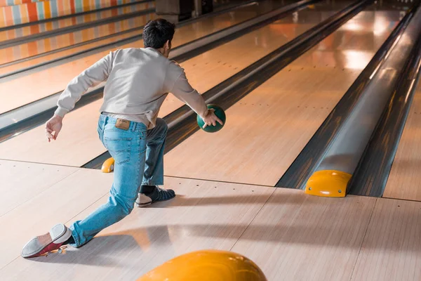 Back view of young man throwing bowling ball on skittle alley — Stock Photo