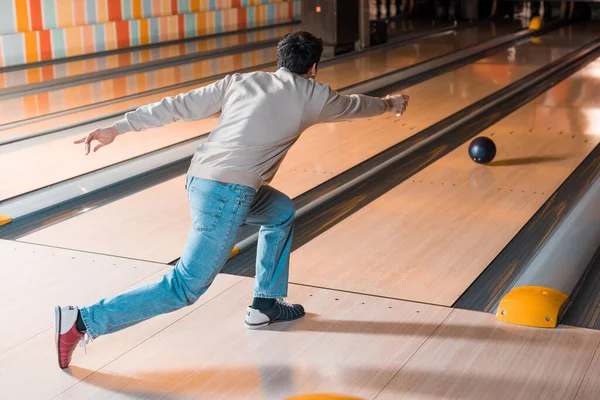 Vue de dos du jeune homme lançant la boule de bowling sur l'allée de skittle — Photo de stock