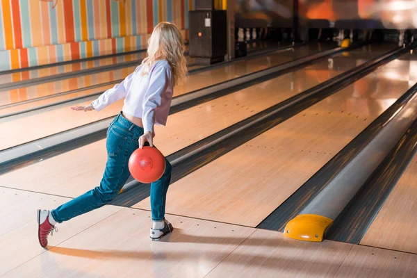 Jeune femme blonde lançant boule de bowling sur ruelle de skittle — Photo de stock