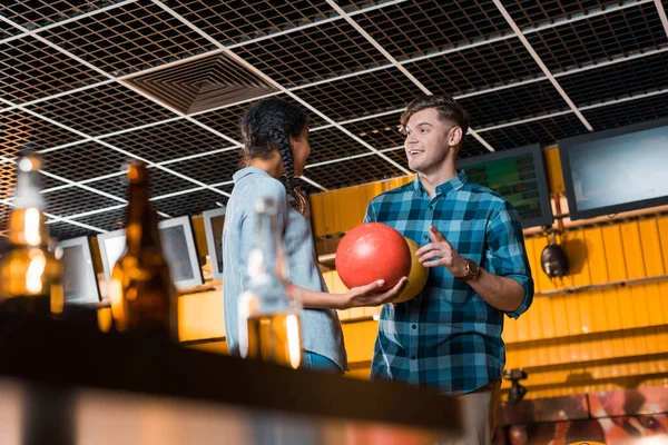 Foyer sélectif de sourire homme parler à afro-américaine fille tout en tenant boules de bowling — Photo de stock