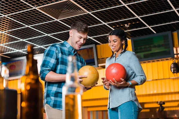 Foyer sélectif de couple interracial parler et sourire tout en tenant des boules de bowling — Photo de stock