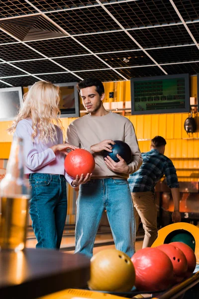 Handsome man talking to blonde girlfriend while holding bowling balls — Stock Photo