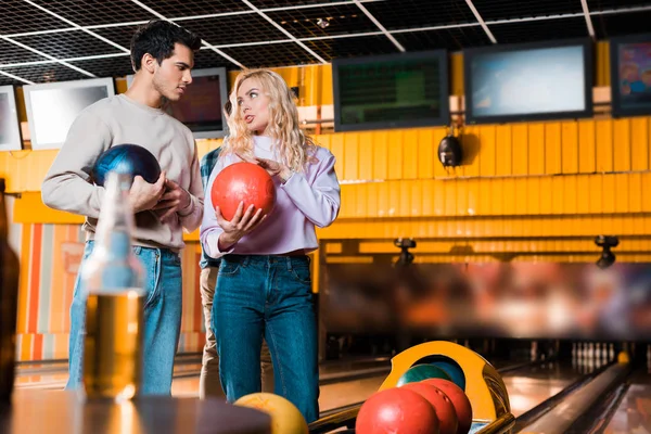 Selektiver Fokus junger Männer und Frauen, die sich beim Halten von Bowlingbällen im Bowlingclub unterhalten — Stockfoto