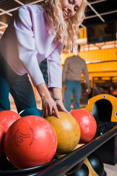 Chica rubia sonriente elegir bola de bolos en el club de bolos - foto de stock