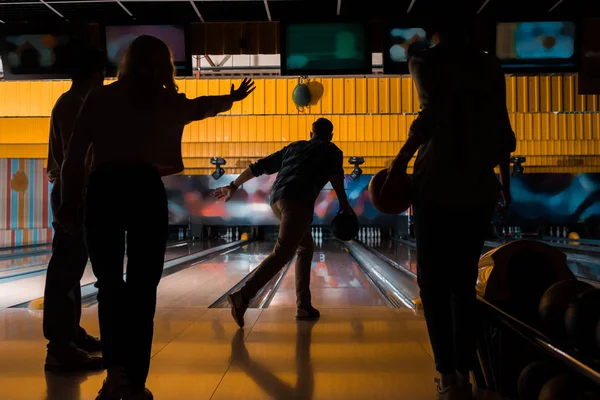 Sagome scure di quattro amici che giocano a bowling nel bowling club — Foto stock