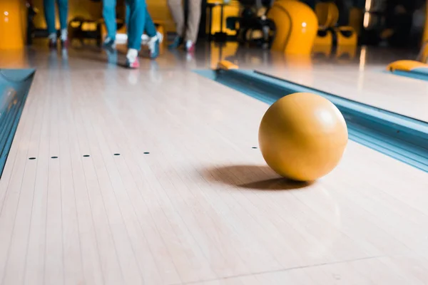 Enfoque selectivo de la bola de bolos en la pista de skittle y amigos de pie en el fondo - foto de stock