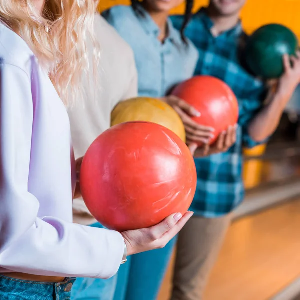 Partial view of multicultural friends holding bowling balls while standing in bowling club — Stock Photo