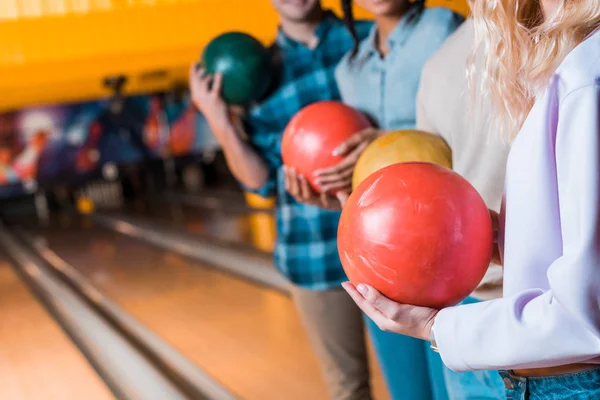 Vista recortada de amigos multiculturales sosteniendo bolas de bolos mientras están de pie en el club de bolos - foto de stock