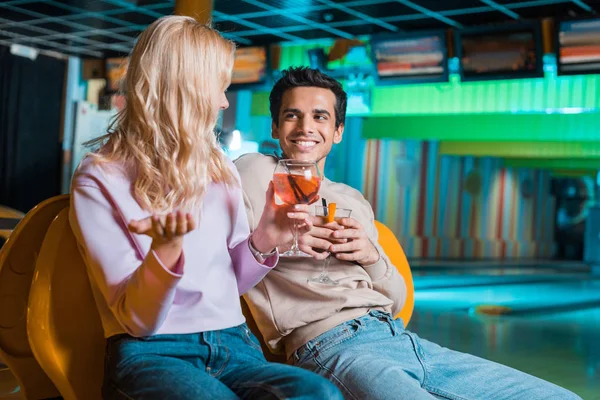 Alegre pareja hablando mientras está sentado en el club de bolos y beber cócteles - foto de stock