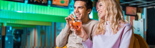 Panoramic shot of cheerful couple sitting in bowling club and drinking cocktails — Stock Photo