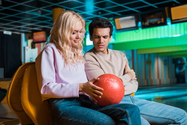 Chica sonriente mostrando bola de bolos a novio reflexivo en el club de bolos - foto de stock