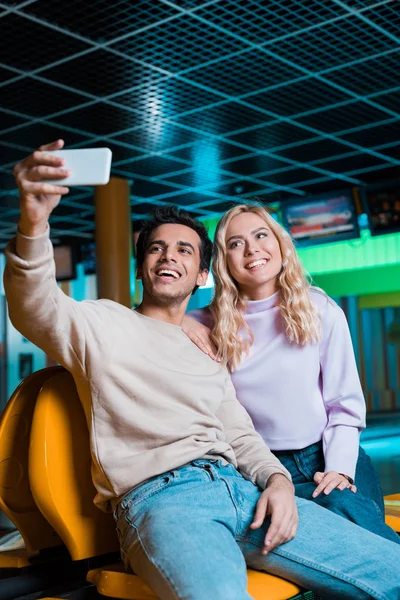 Весела пара бере селфі на смартфон, сидячи в боулінг-клубі — стокове фото