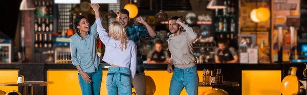 Панорамный снимок счастливых мультикультурных друзей, показывающих жест победителя в боулинг-клубе — стоковое фото