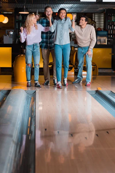 Happy african amerrican girl showing winner gesture while looking at skittle alley near multicultural friends — Stock Photo