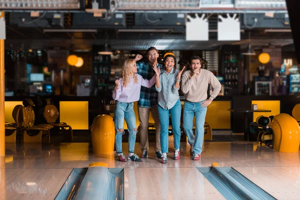 Cuatro alegres amigos multiculturales de pie cerca de la callejuela en el club de bolos - foto de stock