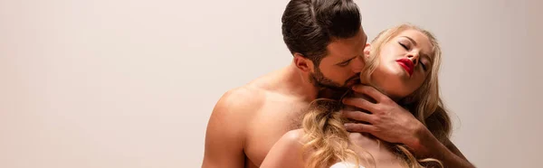 Панорамный снимок красивого и мускулистого мужчины целующегося с сексуальной женщиной, изолированной на серой — стоковое фото