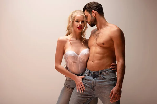 Uomo muscoloso in piedi vicino a donna sexy in jeans su grigio — Foto stock